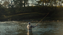 Young fly fisherman casting on a foggy river at sunrise