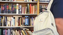 student with a book bag in a library 