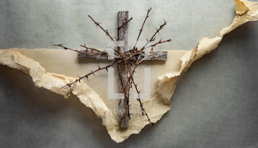 rustic wood cross with thorny stems and a background of torn and crumpled manila paper on a mottled gray surface