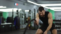 Focused muscular man working out in the gym using battle ropes.