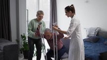 Old man with crutches making first steps with support of wife and doctor.