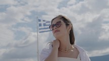 Attractive female tourist with waving Greek flag on the background, slow motion