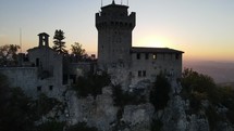 Aerial drone shot ascending in front of medieval tower with sunset behind.