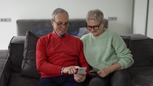 Happy senior couple with smartphone at home.