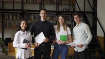 Zoom in rtrait of four multiethnic young people standing together in group looking at camera posing at library or in modern office. Successful business team, students groupmates friends concept.
