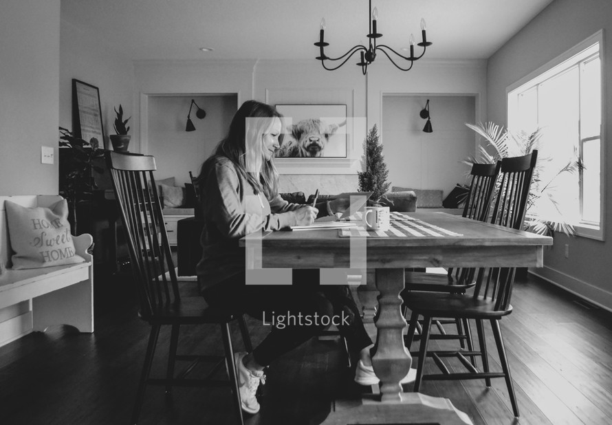 a woman sitting at the kitchen table writing notes 