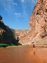 man walking through a river at the bottom of a canyon 