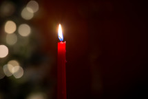 One red melting wax candle burning in front of blurred bokeh Christmas lights