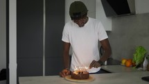 Young black man celebrating his birthday at home, lighting candles.