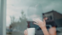 woman holding a coffee cup and looking out a window 