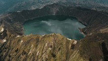 Cinematic aerial view over volcano landscape and crater lake during cloudy day in Ecuador	