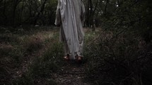 Jesus Christ dressed in white robe, or biblical prophet like Moses, Elijah, Abraham, walking in dramatic slow motion in wooded area surrounded by trees and green grass.