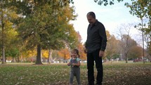 grandfather and granddaughter playing with fall leaves in a park 