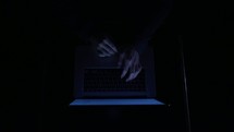 hands typing on a keyboard in the dark 
