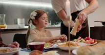 Little girl with braided hair tastes fresh vegetables at the dinner table and tells her dad to salt them with. 