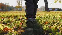 Child feet sneakers walking on fall leaves outdoor. Cute boy walking in the autumn park.