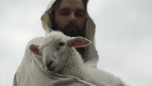 Jesus Christ or a good shepherd of Psalm 23 holds a baby lamb or sheep in his arms.