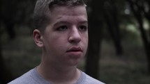 A young, teen boy standing outside in nature in cinematic slow motion.