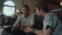 Young Asian antiques dealer showing old pendant and chain to female customer and telling its history in antique store
