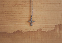 Cross necklace hanging against a stained cardboard background