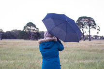 a woman standing outdoors in winter holding an umbrella 