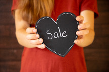 girl holding a black heart with word sale 