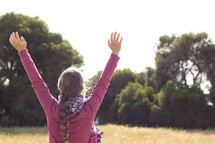 teen girl with braided hair with raised arms standing in a field 