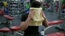 The man sitting and using towel to swipe sweat after finish weight training course at gym.