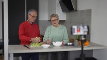 Mature couple cook together, explain recipe and record video for vlog and social media.