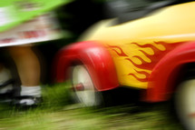 blurry image of wheels of a toddler's toy car and toddler legs