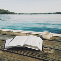 an open Bible and coffee mug on a dock 