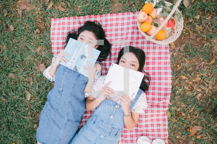 girls lying on a picnic blanket reading books 