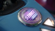 Close-up of a blinking start button on a motorcycle game in an arcade. A girl's hand presses it