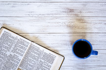Open Bible and coffee mug on a white wood background 