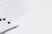 calculator, tacks, and pen on a white desk 