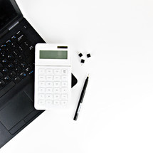 tacks, pen, laptop computer, and calculator on a desk 