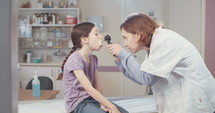 Female doctor examining a sick young girl's throat with an otoscope in the clinic.
