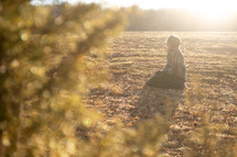 a woman kneeling in prayer in a field 