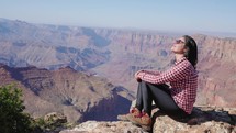 Grand Canyon, Arizona - tourist woman, sitting on a rock contemplating Grand Canyon scenic view

