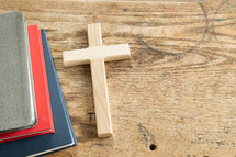red, navy, gray books, and cross on a desk 