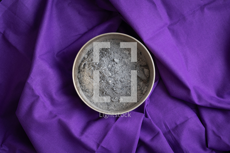 Copper bowl of ashes on a dark purple cloth background shot from above