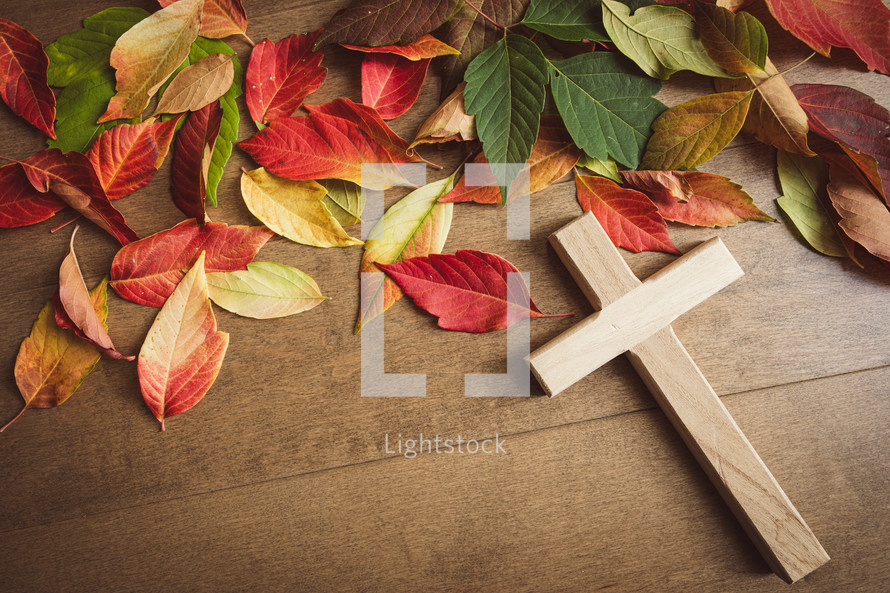 Autumn leaves and wood cross on a light wood background