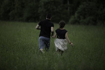 a man and woman running through a field of tall green grasses 