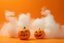 Halloween pumpkins with smoke on orange background, copy space.