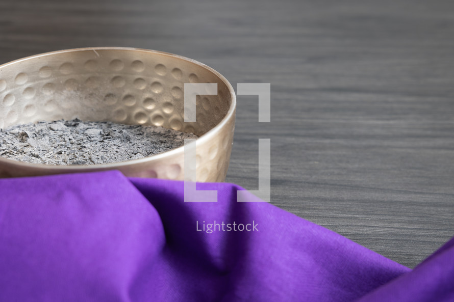 copper bowl of ashes and a purple cloth on a dark wood background