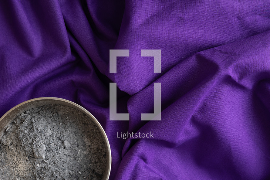 Copper bowl of ashes on a dark purple cloth background shot from above