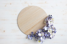 Round light wood board with frame of purple silk flowers on a white background