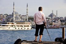 man fishing on a dock across from a mosque