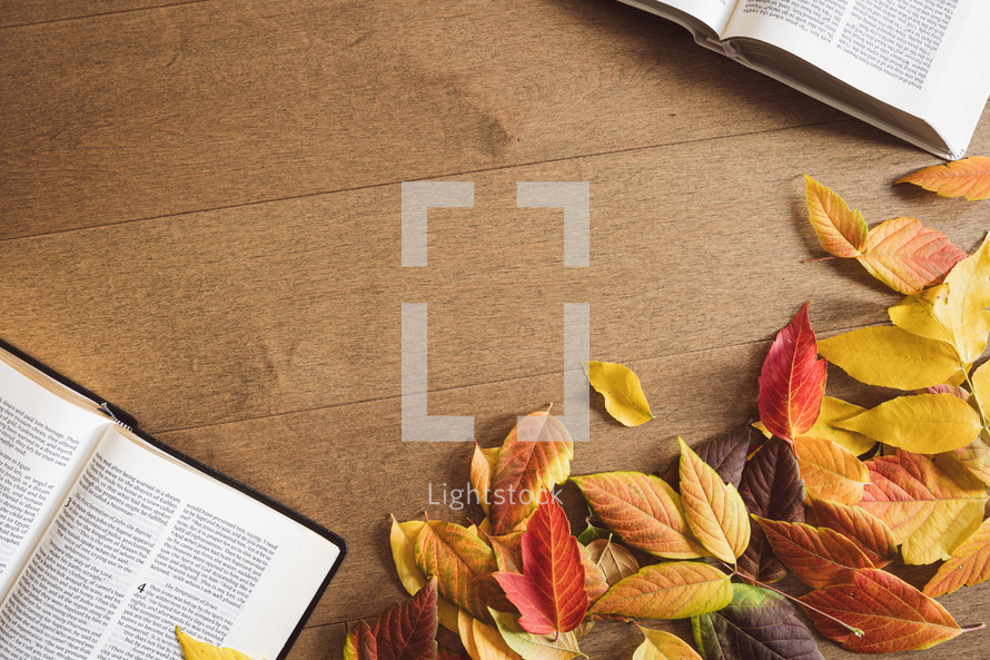 Two open bibles and autumn leaves on a wood table