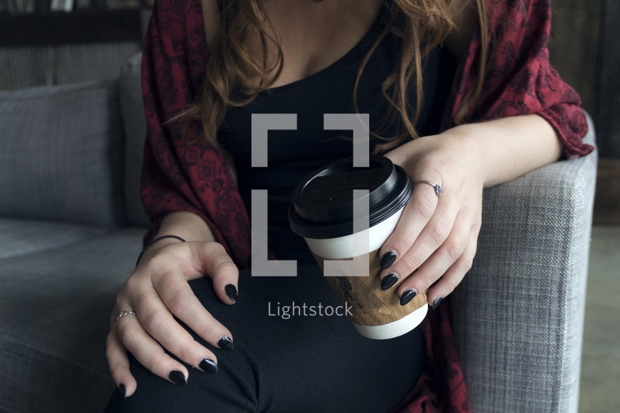 A young woman with black painted nails holding a coffee cup 